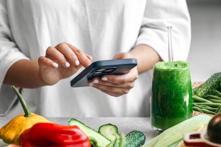 woman-holding-green-detox-smoothie-using-nutrition-app-smartphone-min